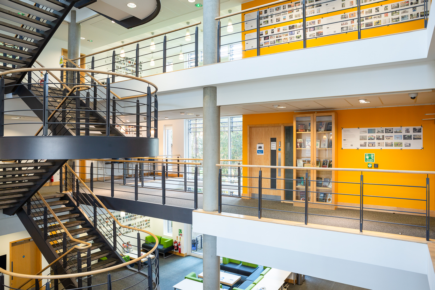 Installation photograph of 'Postcards from Europe' exhibition, postcard-sized photographs printed on long strips of newsprint, displayed across different floors of Art at the ARB, with a staircase featured in the middle of the building.