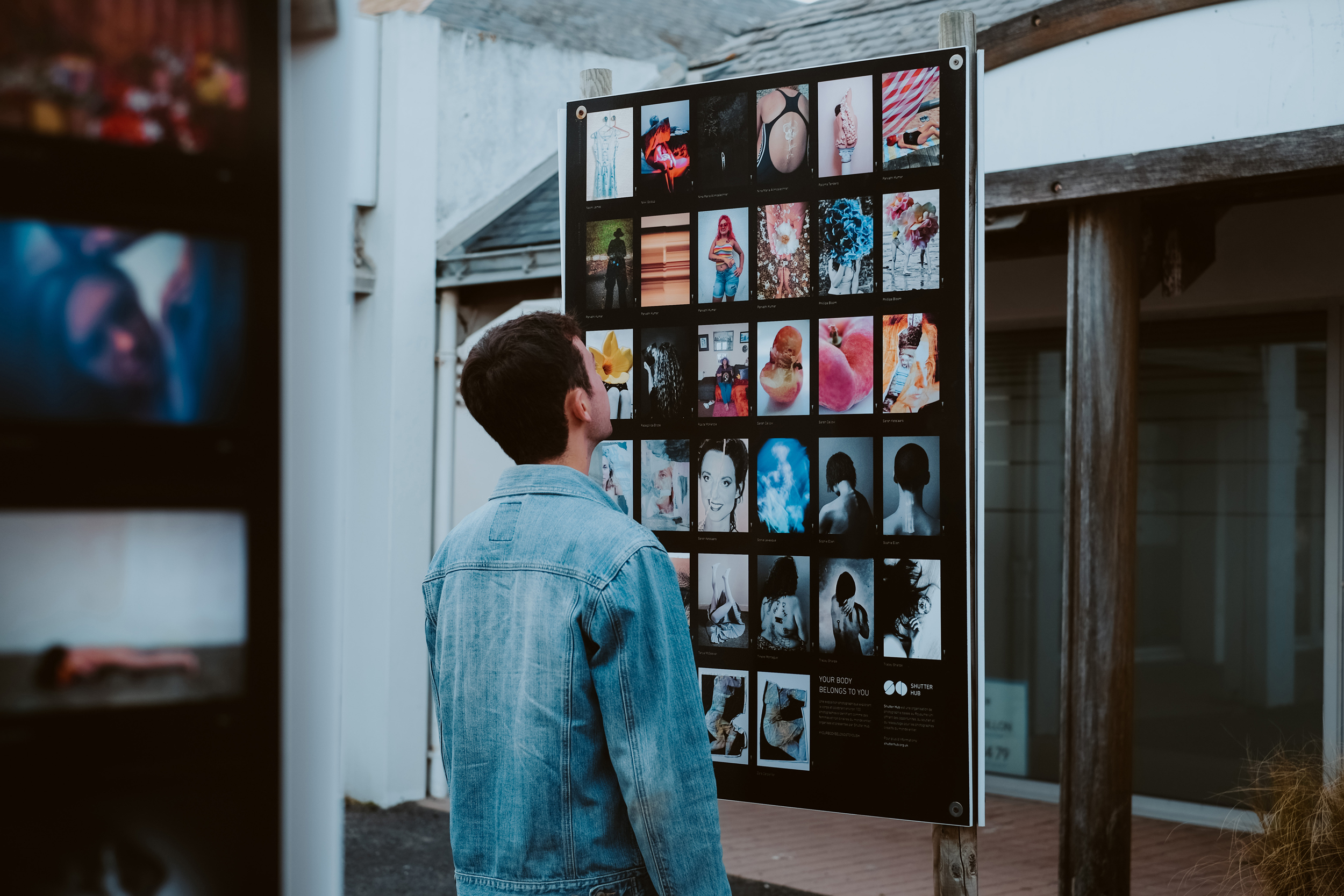 a man in a denim blazer looks at a poster board of exhibition images in an outdoor space