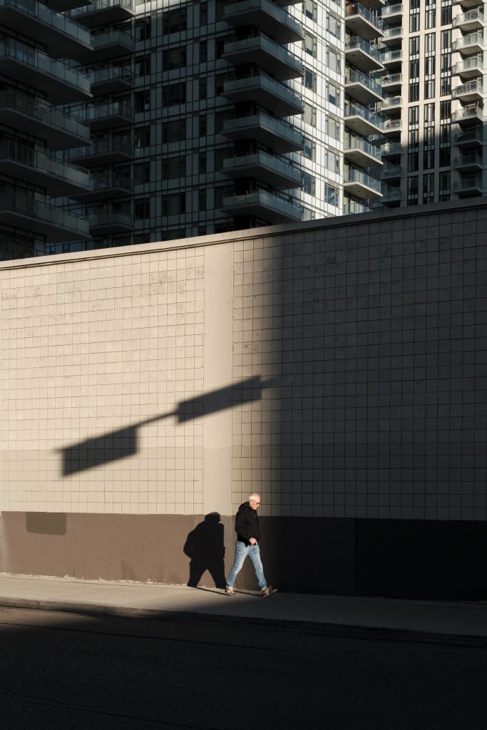 Person walks alone down the street under the shadow of a street lamp and looming buildings.