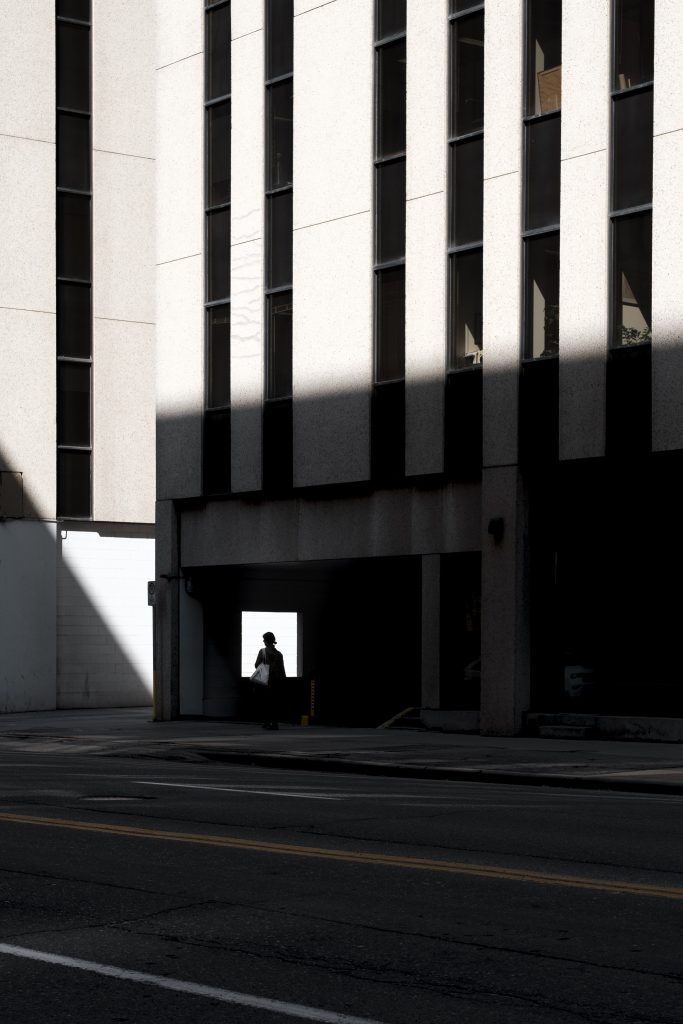 Silhouette of a person on a shadowed downtown street framed by a backlit window frame.
