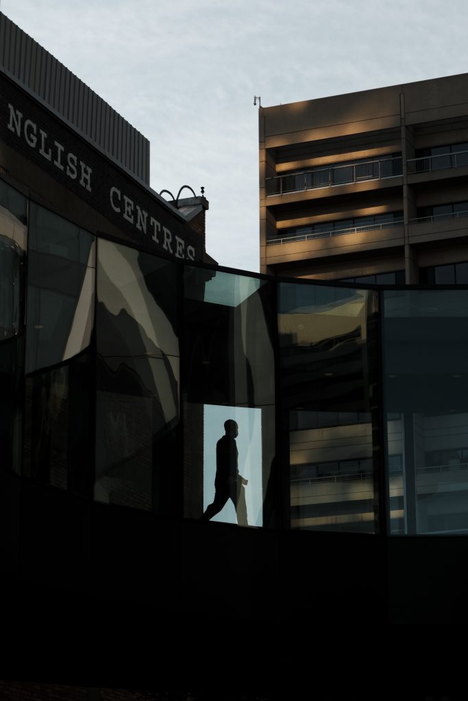 Silhouette of a person walks through elevated downtown walkway as buildings loom behind.