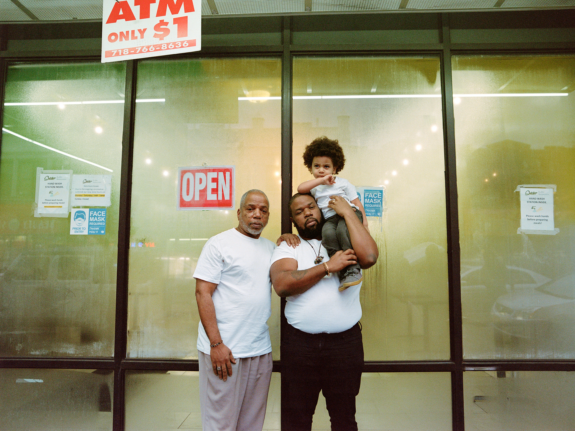 Photograph of three generations, grandfather, father and son standing in front of a shop steamy windows.