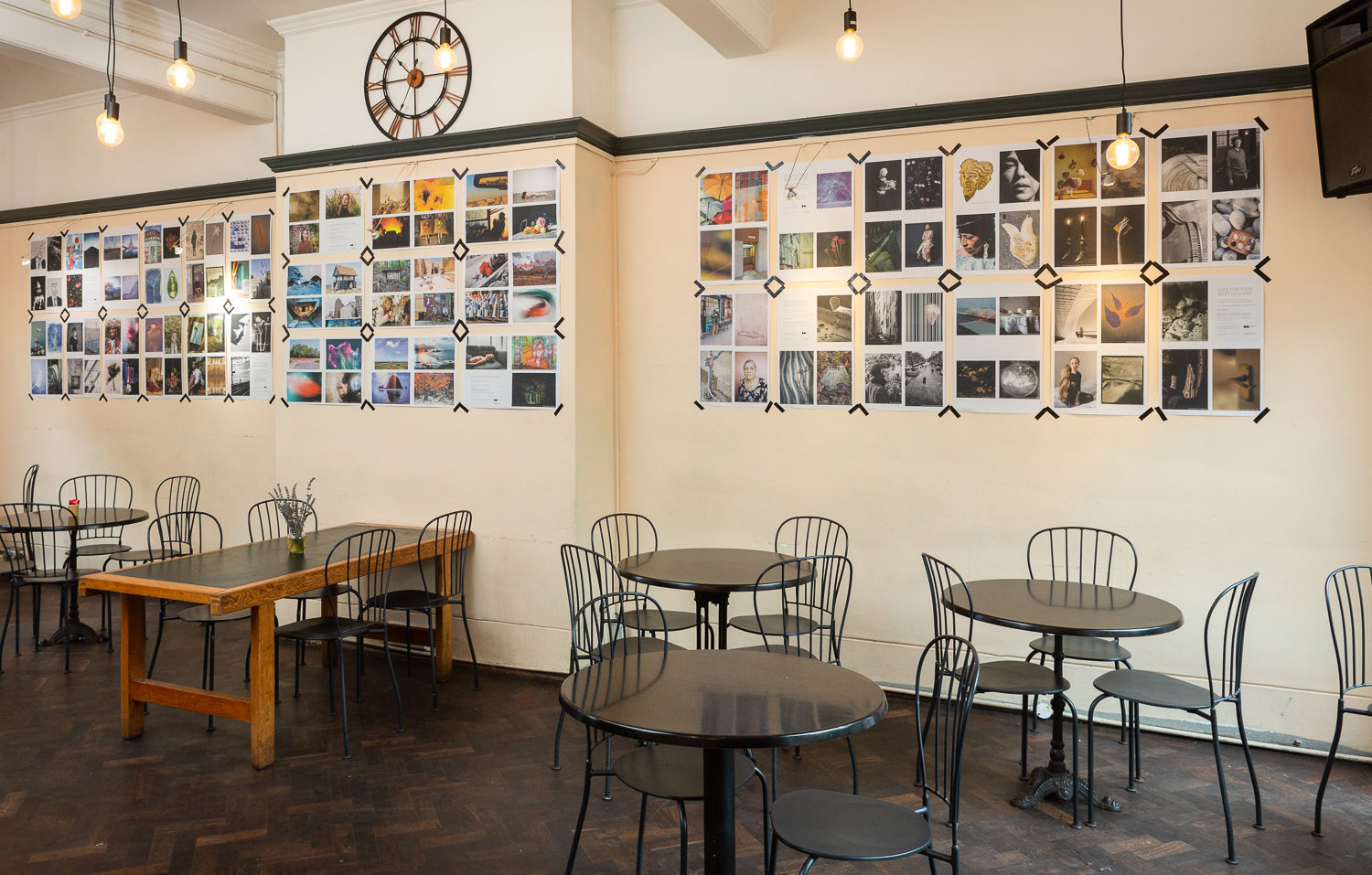 Photograph in the Gallery Café at St. Margaret's House, showing an exhibition of photographs printed on newsprint, tables and chairs in the foreground