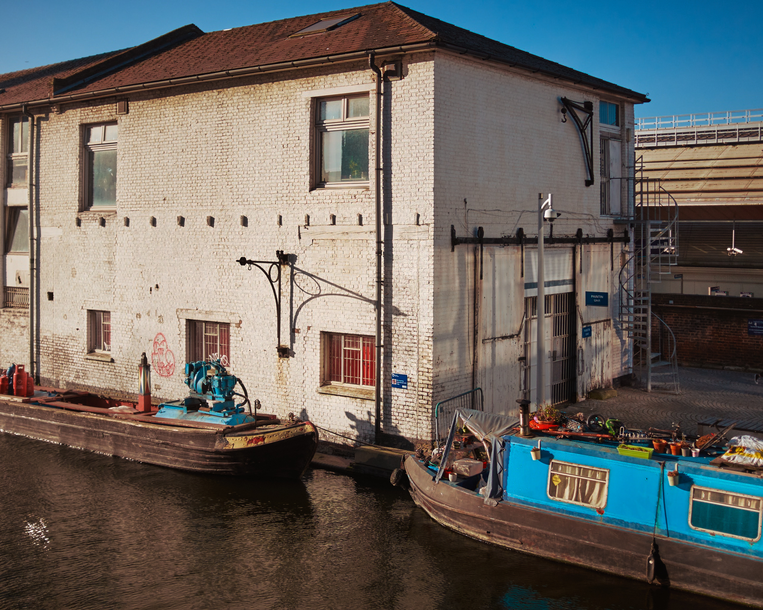 a white building in the sun, with 2 canal boats at the bottom of the frame
