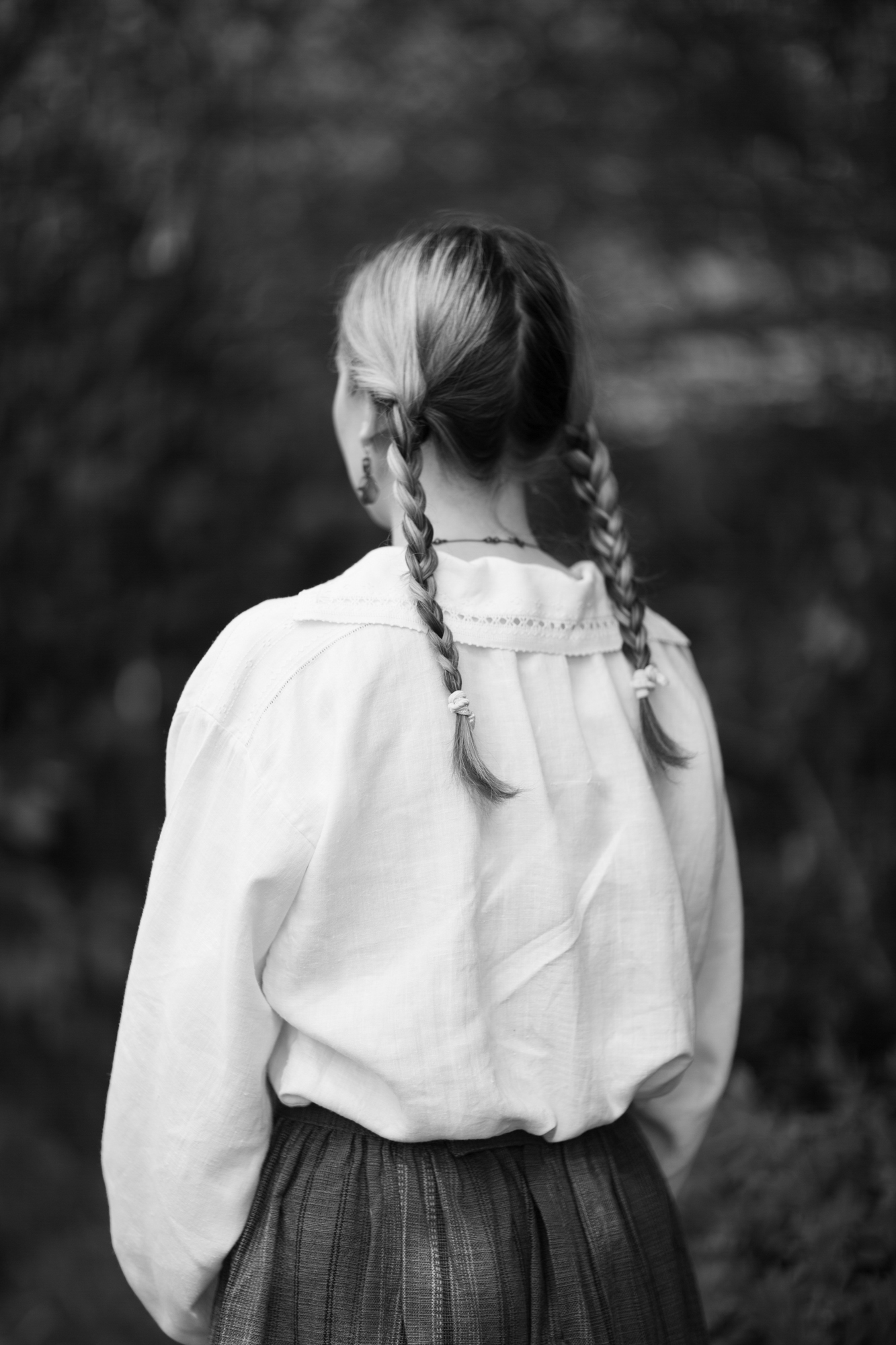 Black and white image of the back of a girl in a white folk blouse with plaits